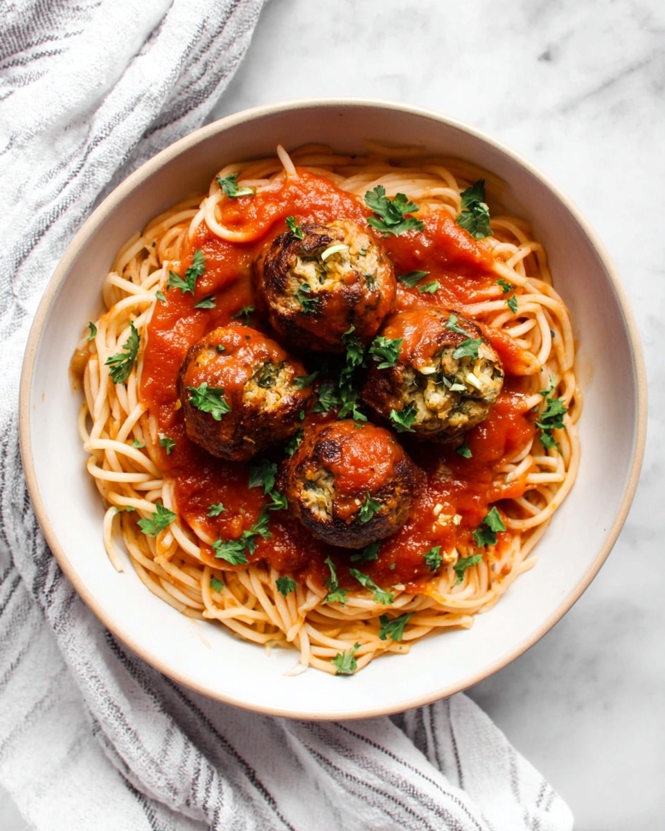 A white bowl filled with a single layer of cooked spaghetti noodles coated lightly with red tomato sauce. On top, there are five round meatballs that are browned and have a slightly crispy texture, each covered partially with the same red sauce. Small green parsley leaves are scattered over the meatballs and sauce for a fresh touch. The bowl is placed on a white marbled surface with a white cloth that has thin gray stripes underneath. photo taken with an iphone --ar 4:5 --v 7