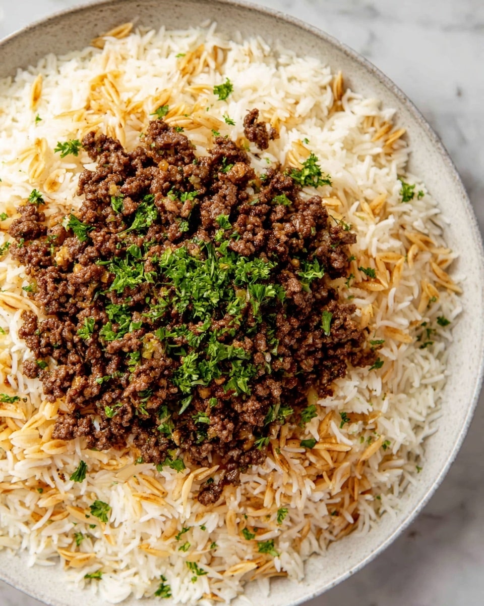 A white plate filled with two layers: the bottom layer is long-grain rice mixed with toasted thin pasta pieces, showing white and golden brown colors and a fluffy texture spread evenly across the plate; the top layer is a mound of cooked ground beef mixed with small pine nuts and finely chopped onions, dark brown in color with a moist, crumbly texture, sprinkled with chopped fresh green parsley for garnish. The plate is placed on a white marbled surface. photo taken with an iphone --ar 4:5 --v 7