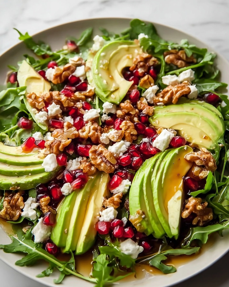 A white bowl filled with a fresh salad featuring a base layer of green arugula leaves covering the whole bowl. On top, there are thin slices of light green pear arranged in a neat semi-circle on one side. Scattered throughout the salad are bright red pomegranate seeds, small crumbles of white goat cheese, and a sprinkling of golden brown chopped walnuts. In the background, half an avocado and a small bowl with more red pomegranate seeds can be seen on a white marbled surface. Photo taken with an iphone --ar 4:5 --v 7