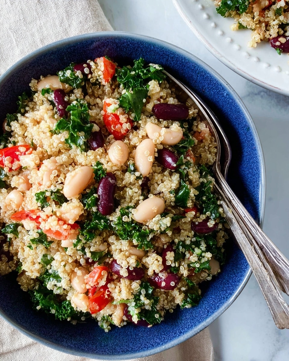 The image shows a close-up of a blue bowl and a white plate filled with a quinoa salad. The salad has three main layers: a base of light beige quinoa grains with a fluffy texture, a mix of white beans and dark red kidney beans scattered evenly, and small pieces of bright red tomato and chopped green kale leaves spread throughout. The quinoa and beans create a grainy, soft texture, while the tomatoes and kale add vibrant color and some crunch. Two vintage silver spoons rest in the blue bowl, placed on a white marbled background with a beige cloth napkin nearby. photo taken with an iphone --ar 4:5 --v 7