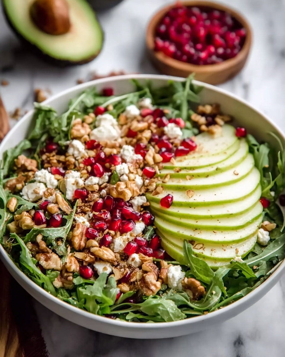 A fresh salad arranged on a white plate, starting with a base layer of dark green arugula leaves that look crisp and leafy. On top are several light green avocado slices with a smooth, creamy texture, placed in a loose circle around the plate. Scattered over these are small, bright red pomegranate seeds that add pops of color and shine. Generous pieces of chunky, brown walnuts are spread evenly, giving a rough texture contrast. Crumbled white cheese bits are sprinkled throughout, adding a soft and crumbly look. The salad is lightly drizzled with a golden dressing that adds a glossy finish. All this sits on a white marbled surface. photo taken with an iphone --ar 4:5 --v 7