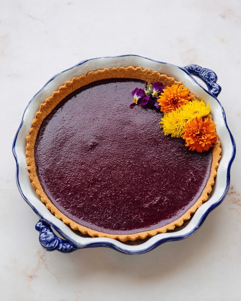 A slice of deep purple pie with a golden, crispy crust forming the bottom and edges sits on a white plate with soft scalloped edges. The pie slice has a smooth, dense texture and is positioned slightly off-center on the plate, with three small, colorful flowers—orange, yellow, and dark red—placed delicately beside it. Nearby, the remaining pie is shown in a white pie dish with blue wavy edges, revealing three missing slices and the same smooth purple filling and crust. The whole scene rests on a white marbled surface, creating a clean and bright setting. photo taken with an iphone --ar 4:5 --v 7