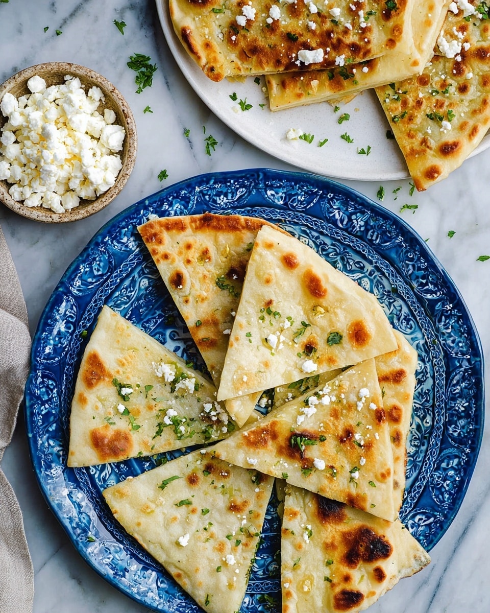 The image shows flatbread cut into triangular slices, arranged in two groups. The first group has four slices stacked lightly over each other on a blue plate with a floral embossed pattern. The flatbread is golden with brown spots from grilling, and small green leaves and white cheese crumbles are scattered on top. The second group is arranged on a white plate, partly visible, with similar slices showing the same golden brown texture and cheese crumbles. Next to this plate, there is another small white plate holding chunks and crumbles of white cheese. The background is a white marbled surface, creating a clean and simple scene. photo taken with an iphone --ar 4:5 --v 7