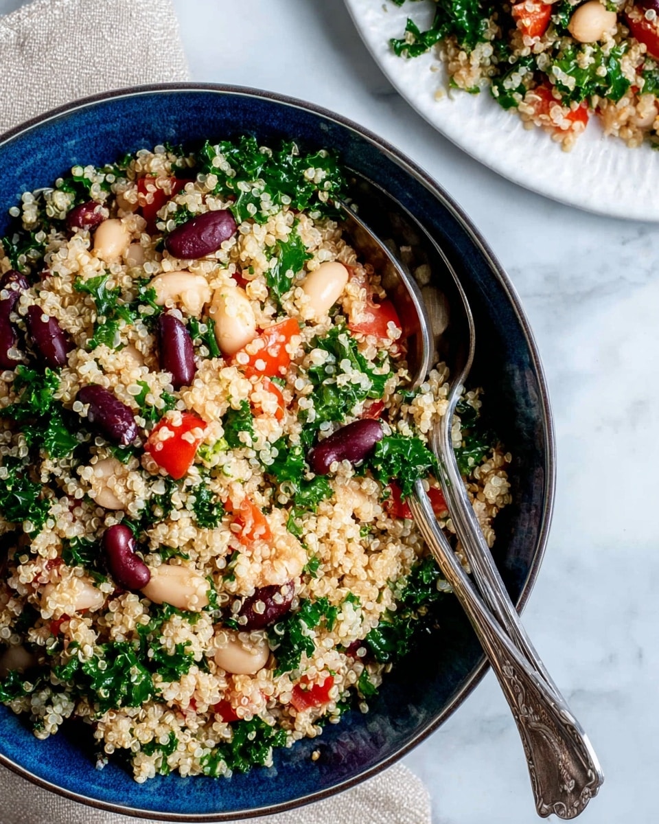 A close-up view of a dark blue bowl filled with a colorful quinoa salad, showing about four layers mixed together: light small quinoa grains, white beans scattered evenly, chunky bright red tomato pieces, and green leafy kale bits all mixed. The textures show the quinoa as soft and grainy, the beans as smooth and plump, the tomatoes juicy and fleshy, and the kale fresh and slightly curly. Two silver spoons partially covered by the salad are placed inside the bowl near the front. The bowl sits on a white marbled surface with a light beige cloth draped on the right side. Photo taken with an iphone --ar 4:5 --v 7