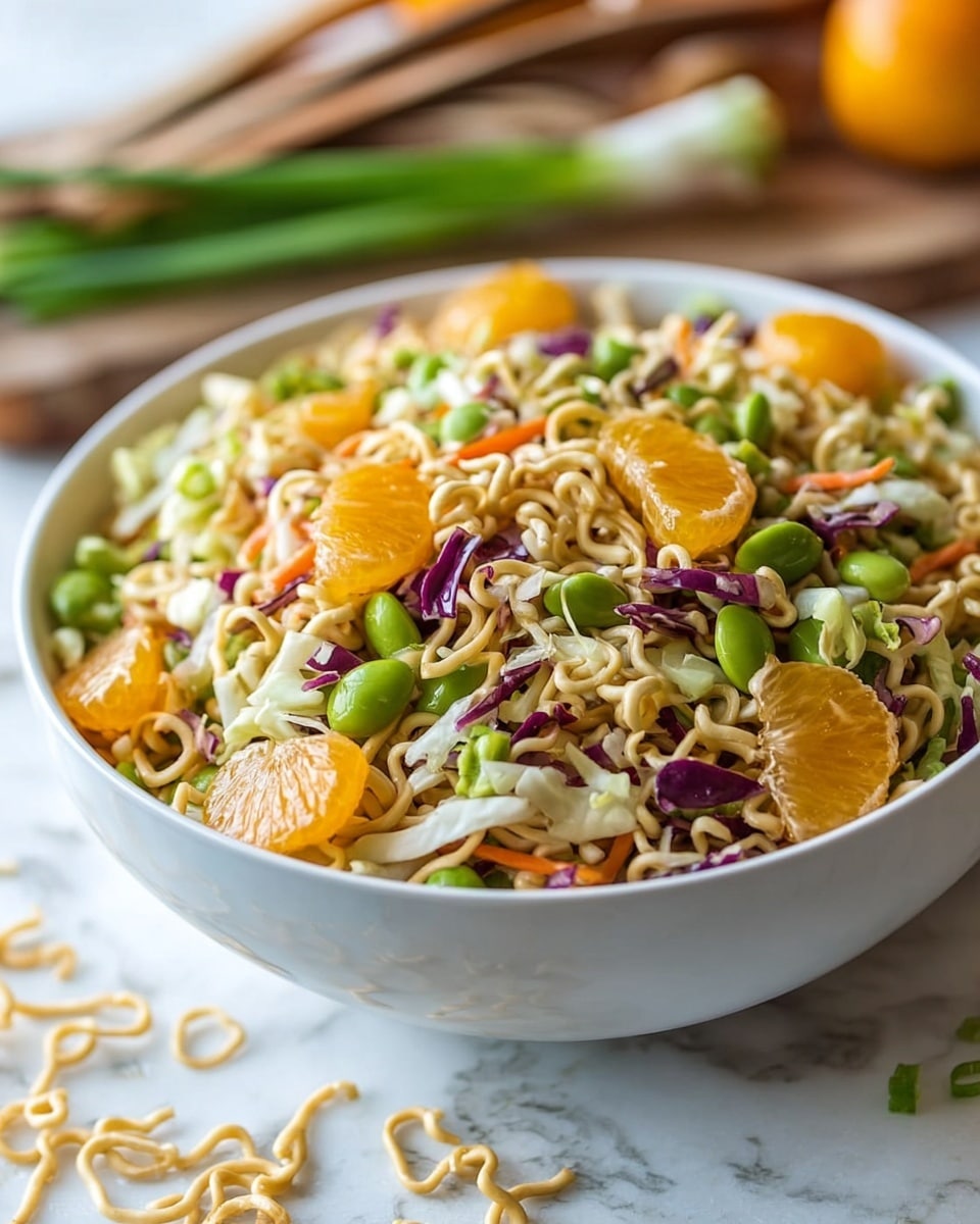 A clear glass bowl on a white marbled surface holds a colorful layered salad mixed with various ingredients. The top layer includes bright orange mandarin slices that add a juicy texture, scattered throughout. There are chopped green onions cut into medium pieces, providing a fresh and crisp touch. Thin, curly pieces of light beige ramen noodles are mixed evenly among the layers. Shredded cabbages in white and purple colors create a crunchy base, accompanied by finely grated orange carrot strips. Edamame beans with a smooth green surface are sprinkled all over. Light brown almond slices and sunflower seeds offer small crunchy accents throughout the salad. Two wooden serving spoons are placed on the side of the bowl. photo taken with an iphone --ar 4:5 --v 7