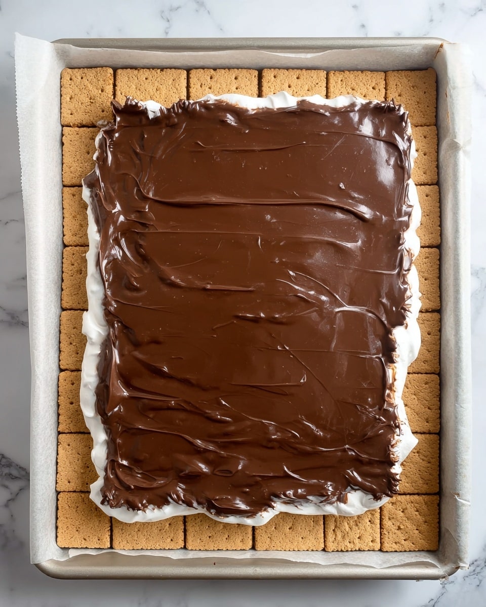 The image shows a dessert in a square baking pan lined with parchment paper, with a white marbled surface underneath. The bottom layer is a grid of light brown graham crackers covering the entire pan. On top of the crackers, there is a layer of white marshmallow cream, mostly covered but slightly visible on the edges. The top layer is a smooth, thick, and glossy melted chocolate spread evenly over the marshmallow cream, with some small uneven ridges and a bit of chocolate dripping over the side. The colors contrast between the light brown of the crackers, white of the marshmallow, and dark brown chocolate. photo taken with an iphone --ar 4:5 --v 7
