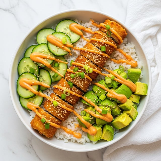 A bowl with a base layer of white rice fills half the bowl, topped with crispy golden-brown fried pieces arranged in a line across the center. On one side of the bowl, neat slices of light green cucumber are placed in a fan shape, and on the other side, chunks of bright green avocado sit in a cluster. The top is generously drizzled with bright orange creamy sauce and sprinkled with chopped green onions and light beige sesame seeds. The bowl is white and sits on a white marbled surface with a white cloth nearby. photo taken with an iphone --ar 4:5 --v 7