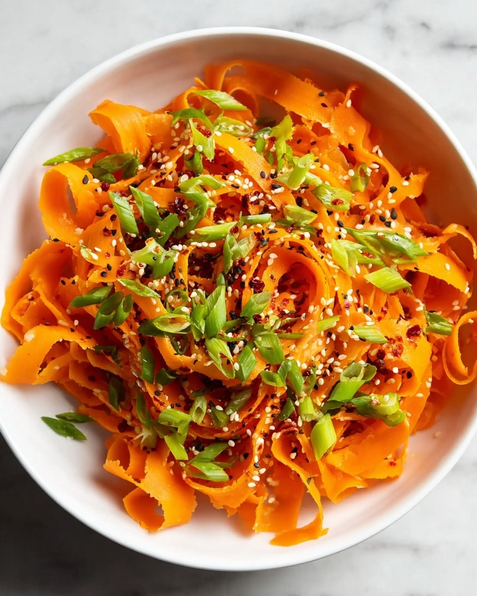 A white bowl filled with thin, curly orange carrot ribbons as the main layer, topped with small bright green chopped scallions evenly spread over the carrots, and sprinkled with white sesame seeds and red chili flakes adding texture and color contrast. The bowl is placed on a white marbled surface, enhancing the vibrant colors of the fresh ingredients. photo taken with an iphone --ar 4:5 --v 7