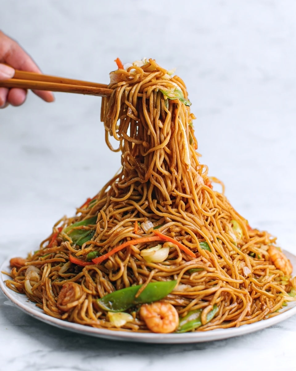 A tall pile of brown noodles mixed with small pieces of green bell pepper, carrots, and shrimp sits on a white round plate on a white marbled surface. A woman's hand is using wooden chopsticks to lift a clump of noodles above the pile, with a few strands dangling down. The noodles have a shiny, slightly oily texture and are tangled together with the vegetables and shrimp visible throughout the dish. photo taken with an iphone --ar 4:5 --v 7