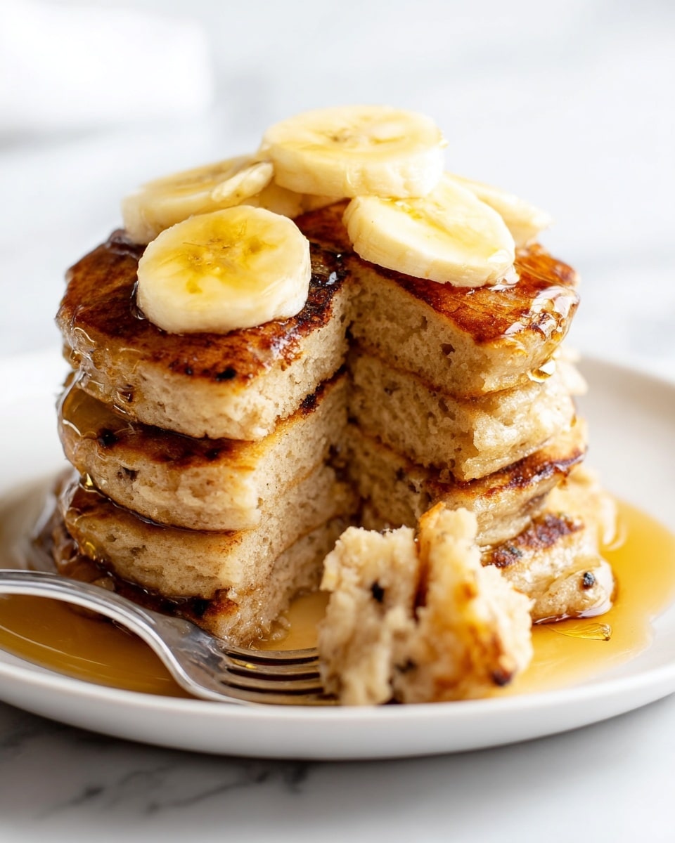 A stack of three golden brown pancakes sits in the center of a white plate, topped with round, soft yellow banana slices. The pancakes have a slightly crispy texture with some darker spots, and the top pancake has a bite taken out, showing the fluffy inside. Amber syrup pools on one side of the plate and drips down the pancakes, with a silver fork holding a bite of pancakes resting on the syrup. Nearby, a white bowl holds more pancakes, similarly browned, and to the left, a small clear glass pitcher contains more syrup. The scene is set against a white marbled surface. photo taken with an iphone --ar 4:5 --v 7