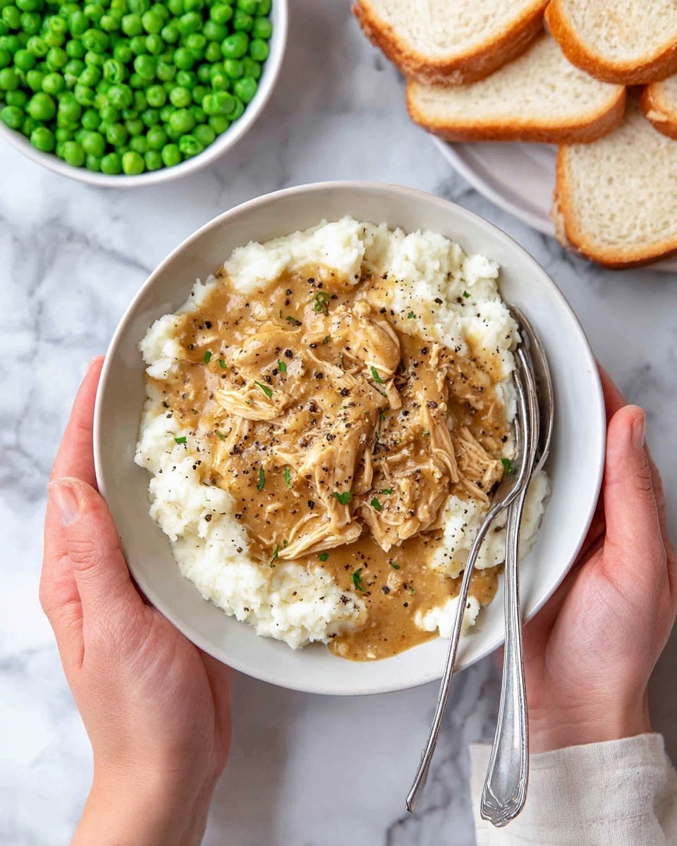Inside a large silver cooking pan, there is a thick, smooth golden brown sauce covering the bottom layer. On top of the sauce, there are shredded pieces of light-colored cooked chicken, some with a slight char or browned texture. A woman's hand holding red-tipped metal tongs is seen mixing the chicken into the sauce, with some chicken pieces lifted slightly above the sauce surface. The pan sits on a stove with black grates, and the surroundings have a clean white marbled texture. photo taken with an iphone --ar 4:5 --v 7