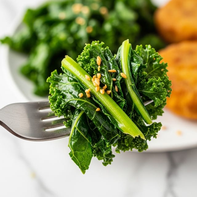 The dish shows a white plate with two main layers: on the left side, a heap of dark green cooked leafy kale with some red chili flakes scattered on top, giving slight color contrast and texture; on the right side, a thick, rectangular piece of grilled salmon with a rich, orange-brown crust showing char marks and seasoning, giving it a slightly rough texture; a silver fork rests near the salmon on the plate, which is set on a white marbled surface with a white cloth underneath. Photo taken with an iphone --ar 4:5 --v 7