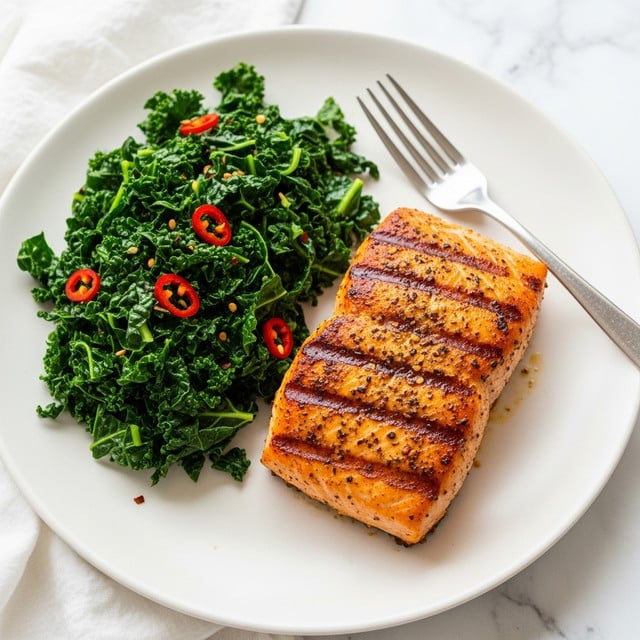A close-up view of a silver fork holding a small bunch of cooked, dark green kale leaves with some pieces showing light green stems and small yellowish seed flakes scattered on top. The kale looks tender and slightly glossy. In the blurred background, there is a white plate with more kale and a piece of golden brown fried food visible on the right side. The whole scene is set against a white marbled texture. Photo taken with an iphone --ar 4:5 --v 7