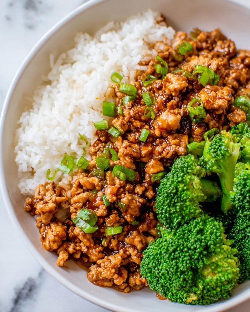 The dish is served in a white bowl on a white marbled surface, showing three main layers: the top layer consists of small green sliced scallions scattered over a glossy, brown, saucy ground meat mixture with a slightly chunky texture. Beneath the meat, there is a layer of fluffy white rice, with visible grains that look soft and separate. On the side, bright green steamed broccoli florets add a fresh contrast with their dense, textured appearance, completing the plate. photo taken with an iphone --ar 4:5 --v 7
