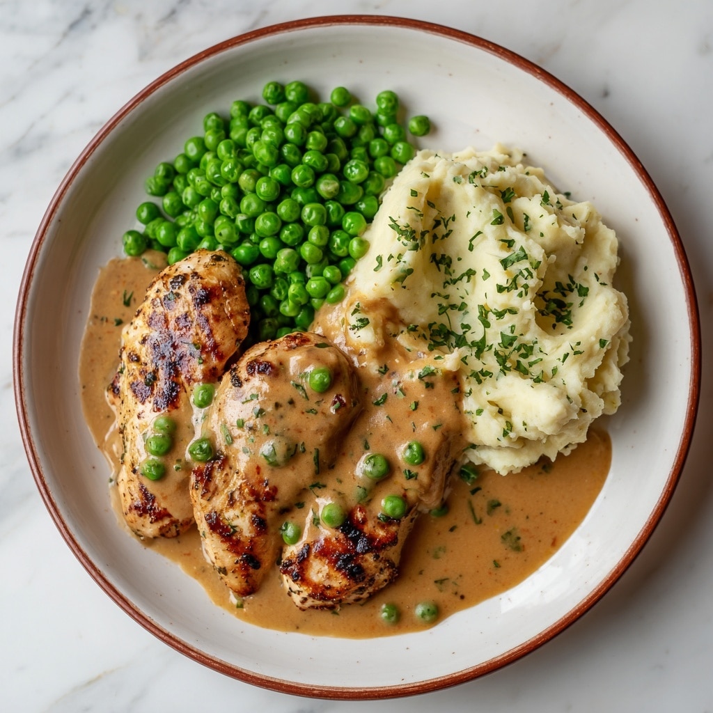 A white round plate on a white marbled texture holds a meal with three main parts. On the left, there is a pile of bright green peas, round and shiny. Next to the peas, on the top right side, there is a creamy white mashed potato portion garnished with small bits of green herbs. The bottom half of the plate shows three pieces of grilled chicken breast covered in a thick light brown sauce sprinkled with several green peas, the chicken having golden brown grill marks and a moist texture. photo taken with an iphone --ar 4:5 --v 7